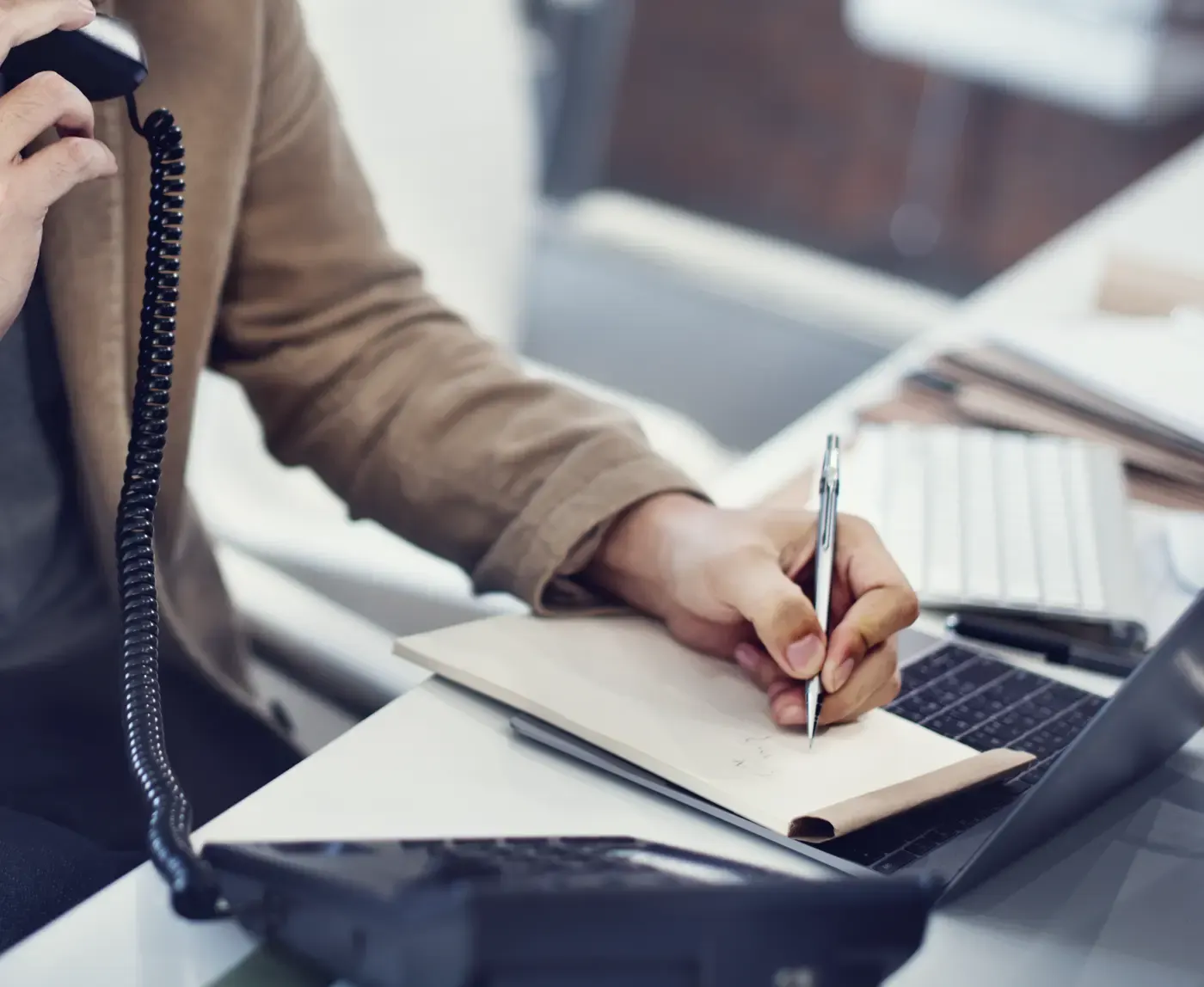 Prise de notes pendant un appel, combiné en main, à côté d'un poste téléphonique
